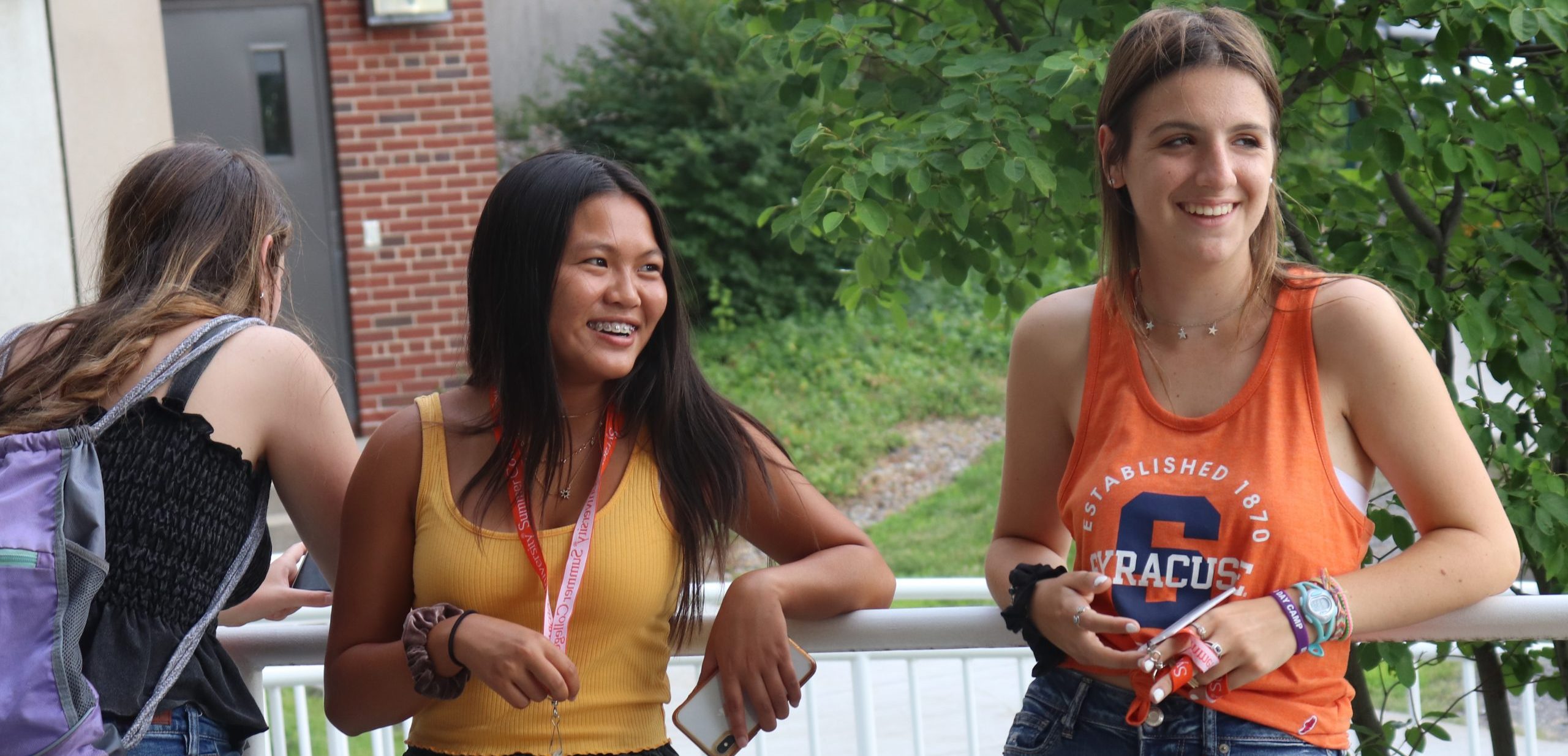 Two high school students wearing Syracuse University shirts and lanyards laugh together.