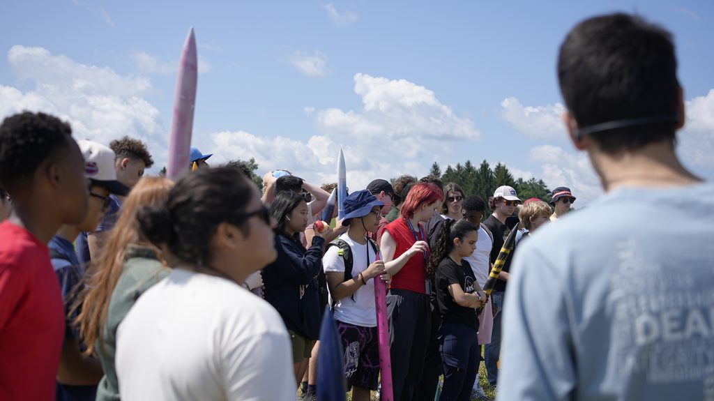 Summer College students participate in an Aerospace Engineering class outside on a large field.