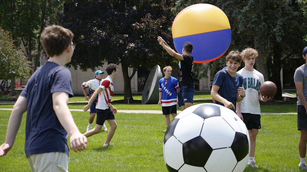 Summer College students tosses giant inflatable balls on a field.