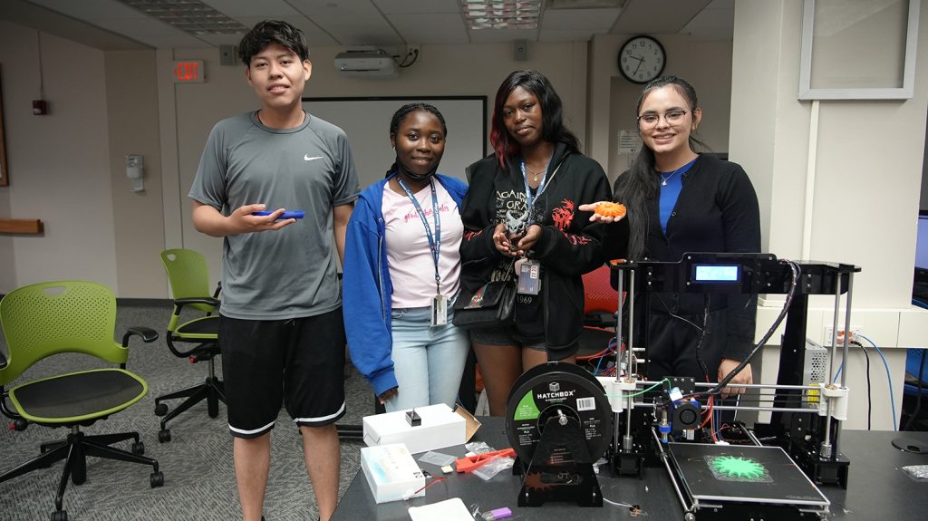 Four Summer College students pose with a 3D printer. 